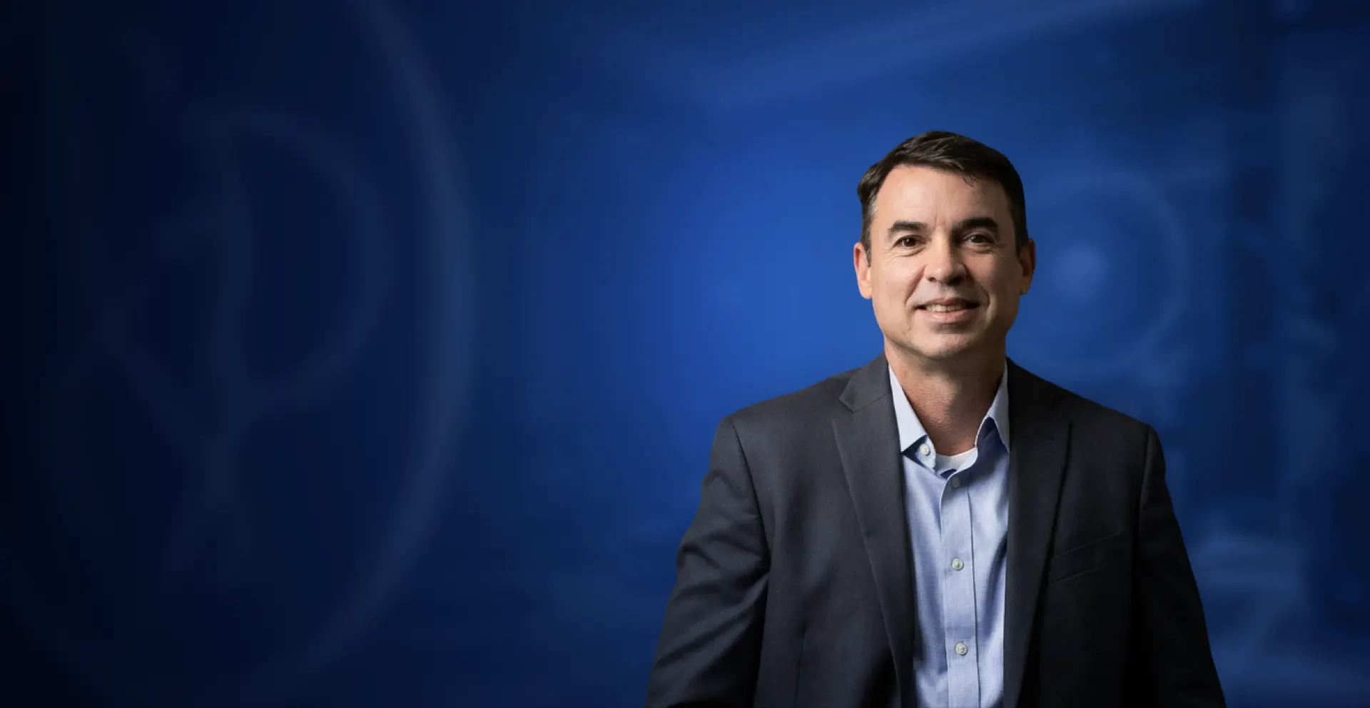 Dr. Edson Prata Jr., cirurgião plástico, sorrindo de terno e camisa azul